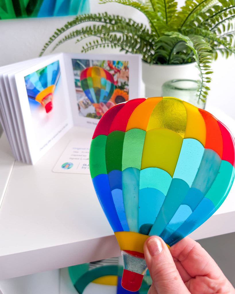 Colorful fused glass art hot air balloon with photobook and plants.