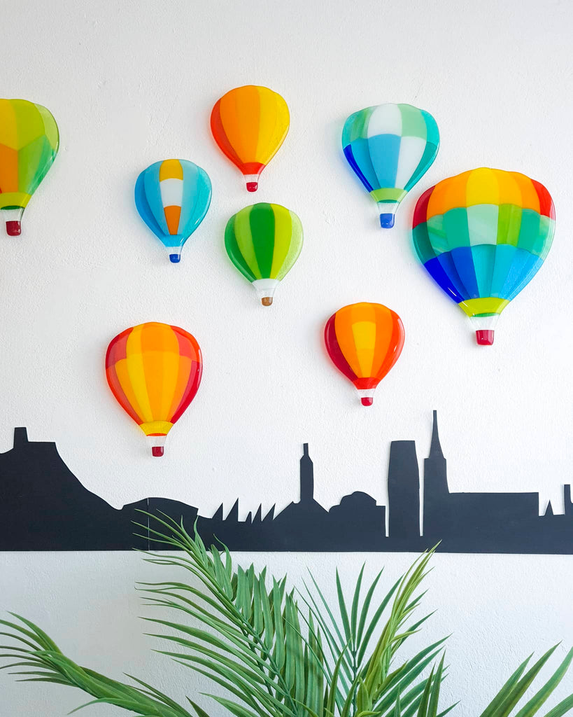 Series of twelve fused glass miniatures depicting colourful hot air balloons, each with unique designs in vivid colours