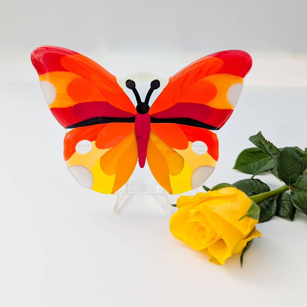 Fused glass art butterfly next to a yellow rose on a white background