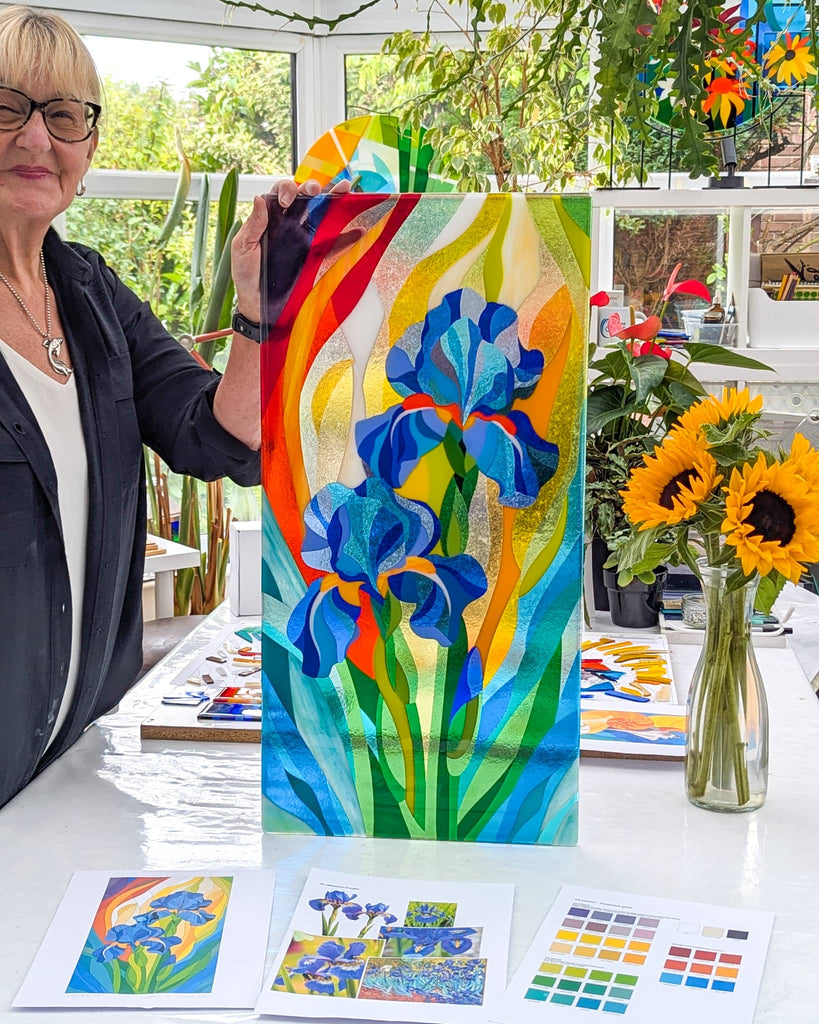 Linda Rossiter presenting a commissioned Hard Edge fused glass panel with blue irises, bespoke contemporary glass art in studio setting
