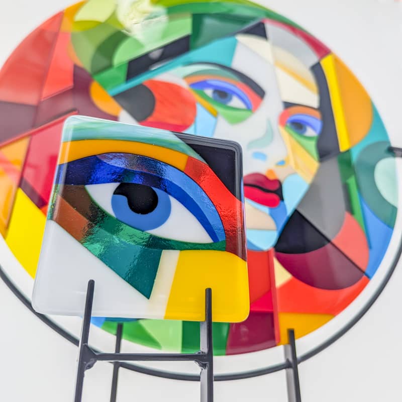 Hard Edge fused glass portrait roundel with abstract face design and miniature glass panel featuring colourful eye, contemporary glass art by Linda Rossiter