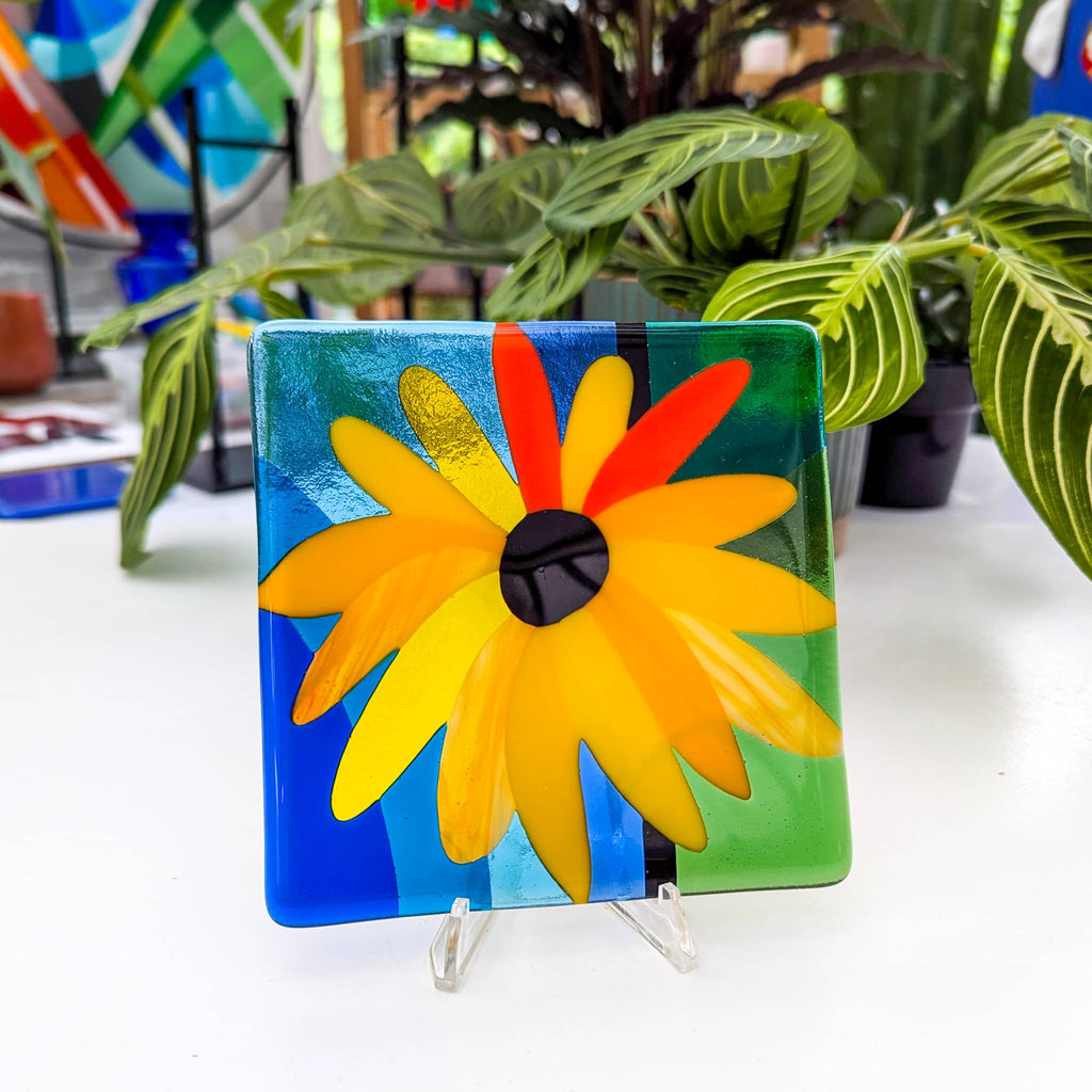 'Abundance' fused glass Miniature with a sunflower design on a stand, surrounded by plants.