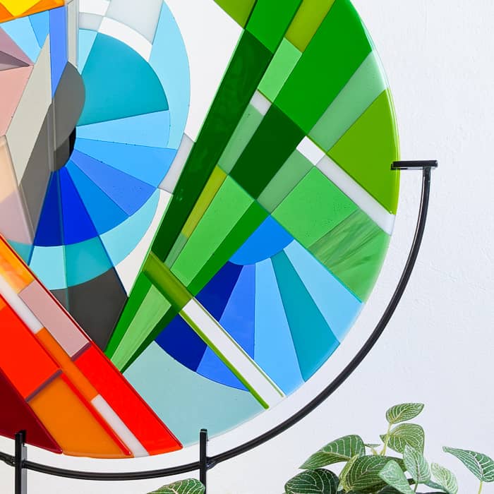 Close-up of 'Stairs' contemporary Hard Edge glass roundel showing intersecting green forms, blue spiral elements and geometric composition