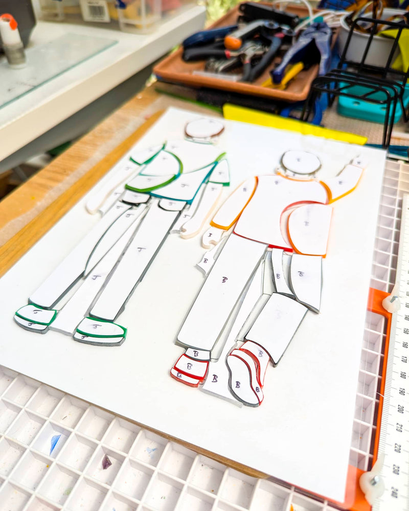 Commissioned contemporary glass Miniatures in progress showing individually cut glass pieces arranged before firing to create two grandson figures
