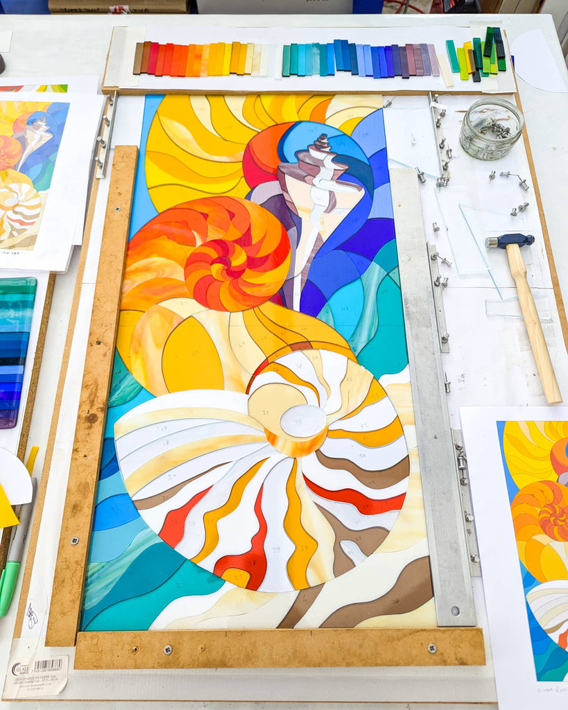 Work in progress Hard Edge fused glass panel with nautilus shell design, colourful cut glass pieces assembled on template during commission by Linda Rossiter