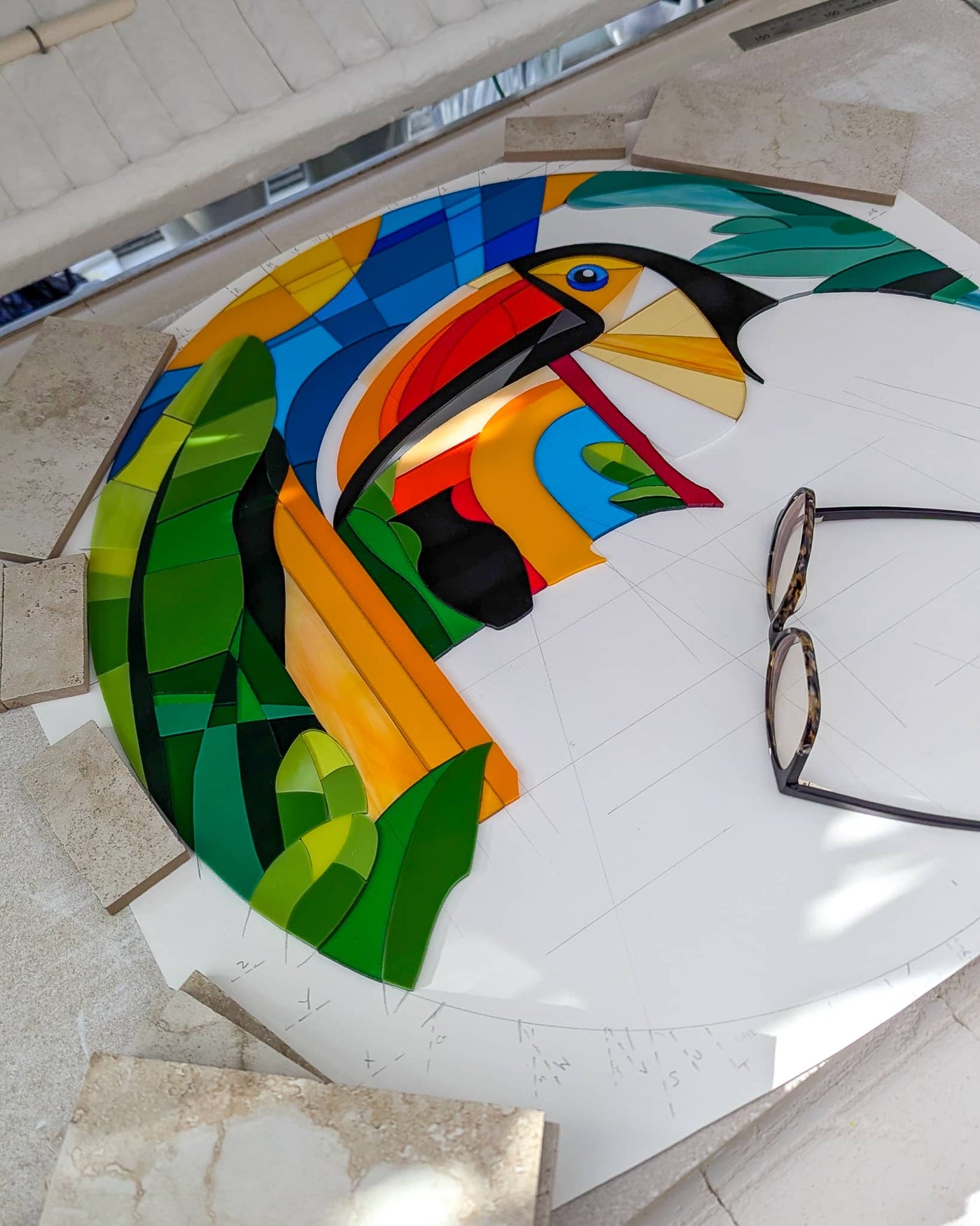 Work in progress on the 'Toucans' contemporary Hard Edge glass roundel showing individually cut glass pieces carefully positioned on the kiln shelf before firing, with the remaining sections still to be completed