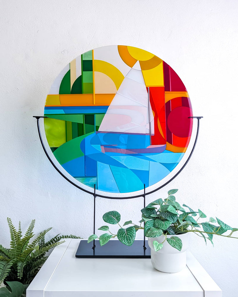 Beaulieu River Hard Edge fused glass roundel with a scow sailboat, river landscape and bold geometric colours