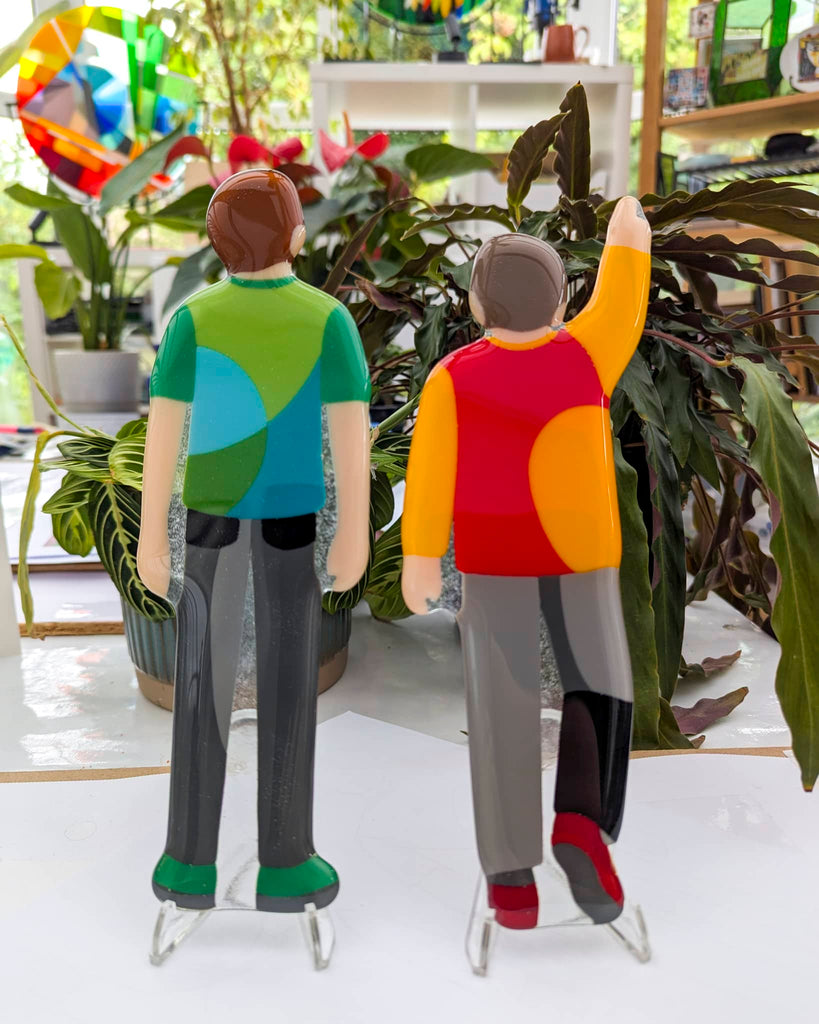 Two colourful fused glass figurines of young boys, representing a commissioned artwork to celebrate family milestones – created by Glass Art by Linda