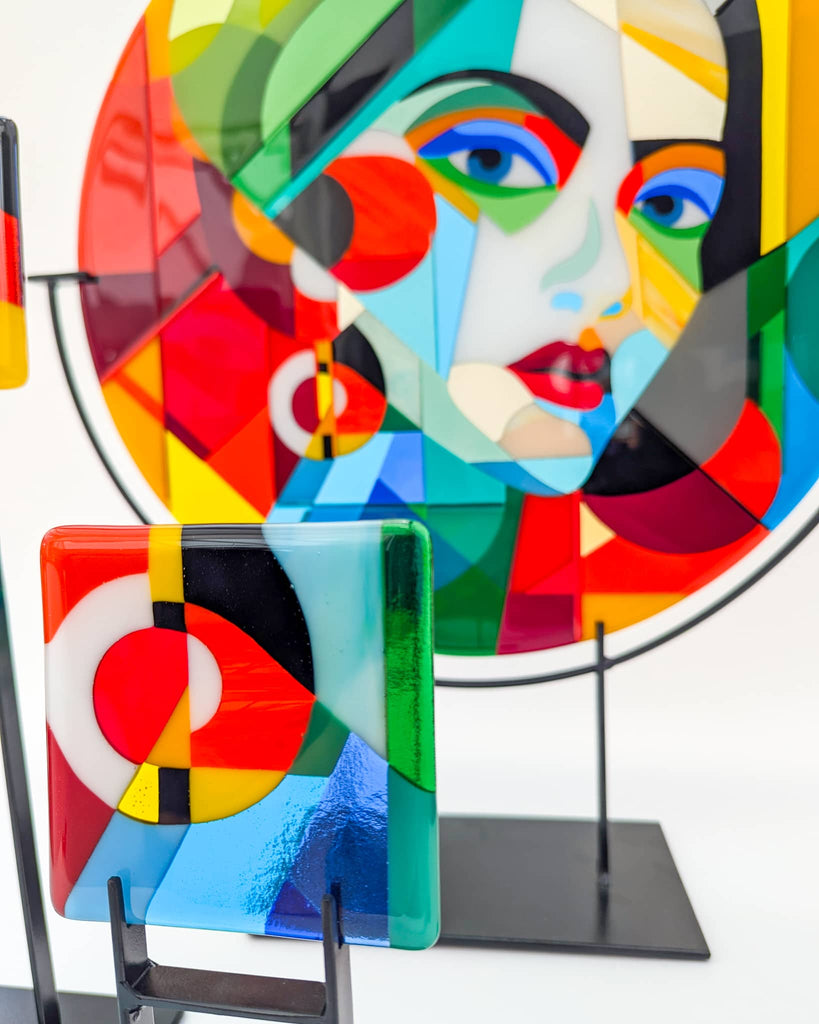 Bold and colourful fused glass artworks on stands, including a large round portrait and a smaller abstract panel – commissioned statement pieces from Glass Art by Linda