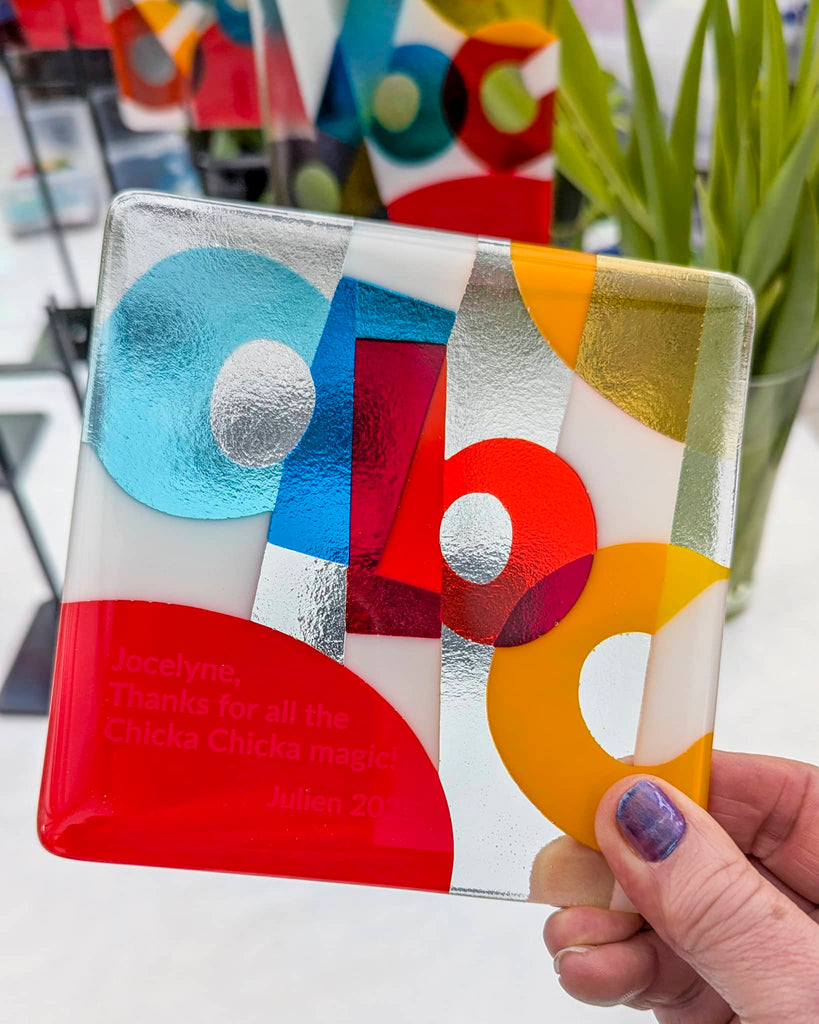 Hand holding a small square fused glass artwork in bright geometric colours, inscribed with a personal thank-you message – a commissioned piece from Glass Art by Linda