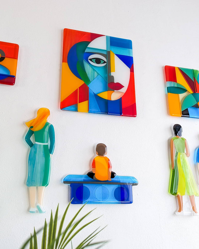 Closer view of Gallery showing colourful fused glass figures, a seated person and abstract pictures arranged on the wall