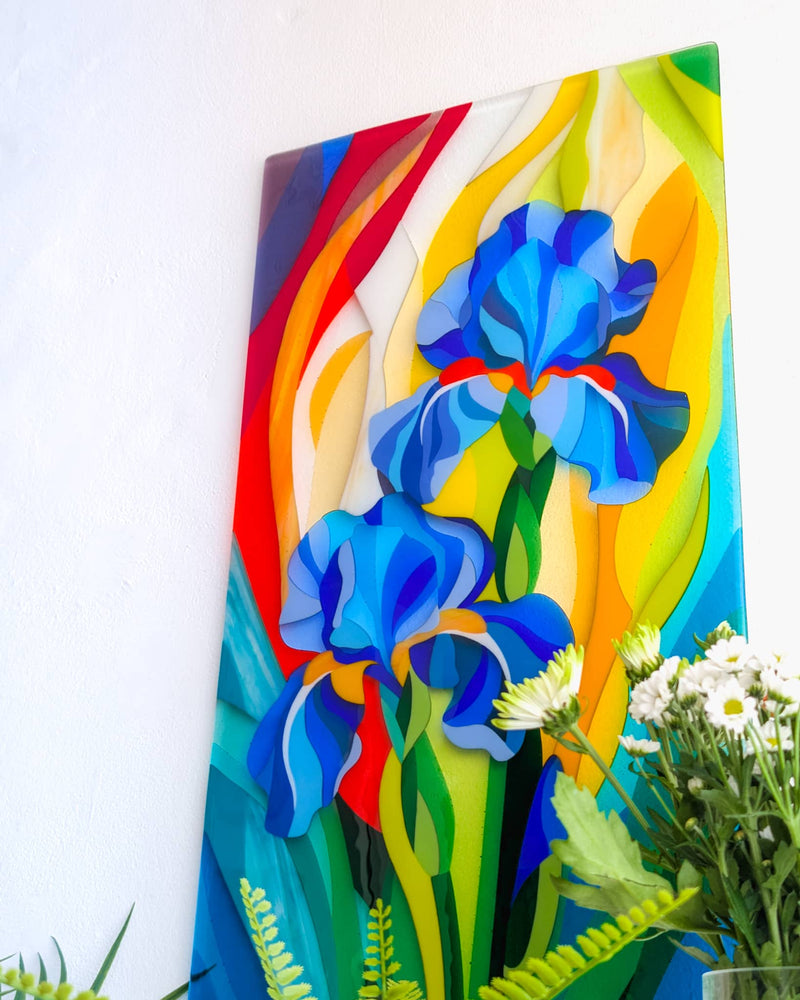 Angled view of the Gardening glass wall panel showing blue irises surrounded by sweeping red, yellow, green and turquoise shapes