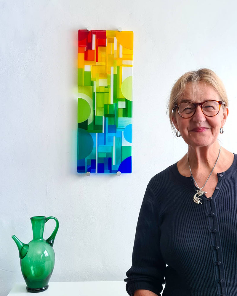 Linda Rossiter standing beside the narrow colourful glass wall panel Spectrum