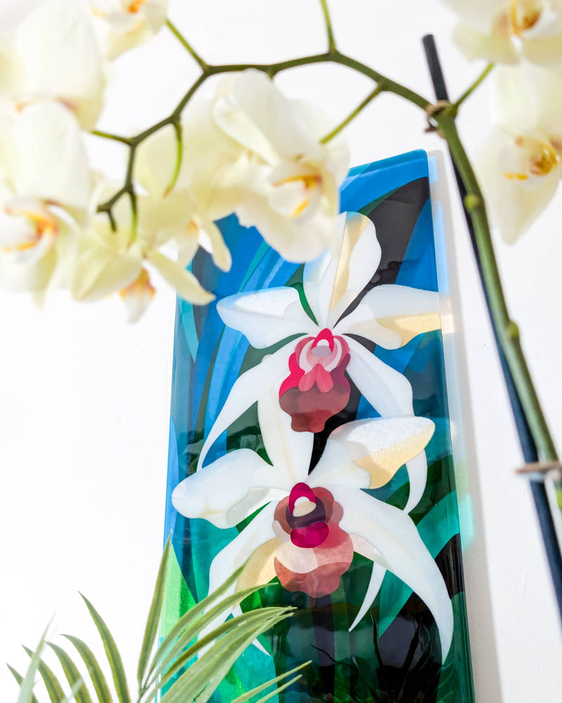 Angled view of the tall Orchids glass wall panel framed by white flowers and palm leaves