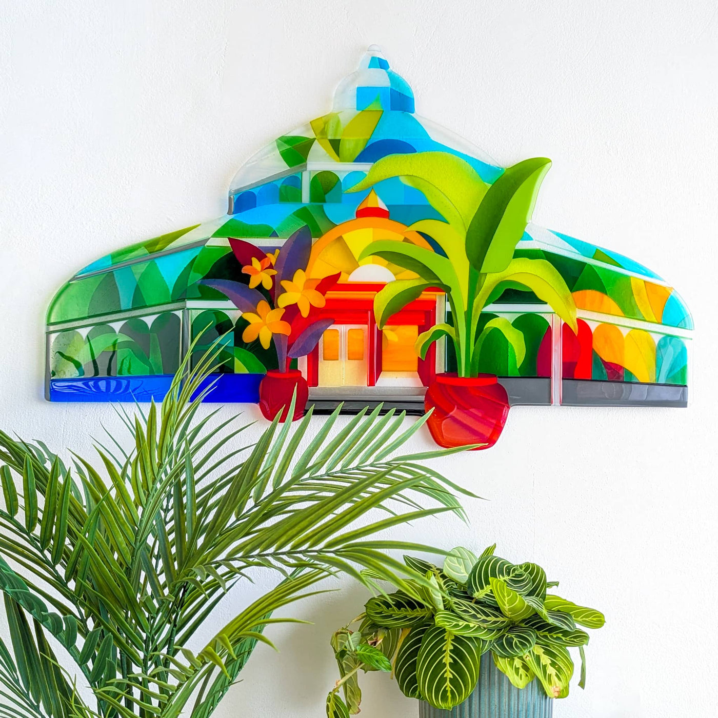 'Palm House' contemporary Hard Edge glass artwork displayed on a wall surrounded by houseplants, echoing the botanical inspiration behind the design