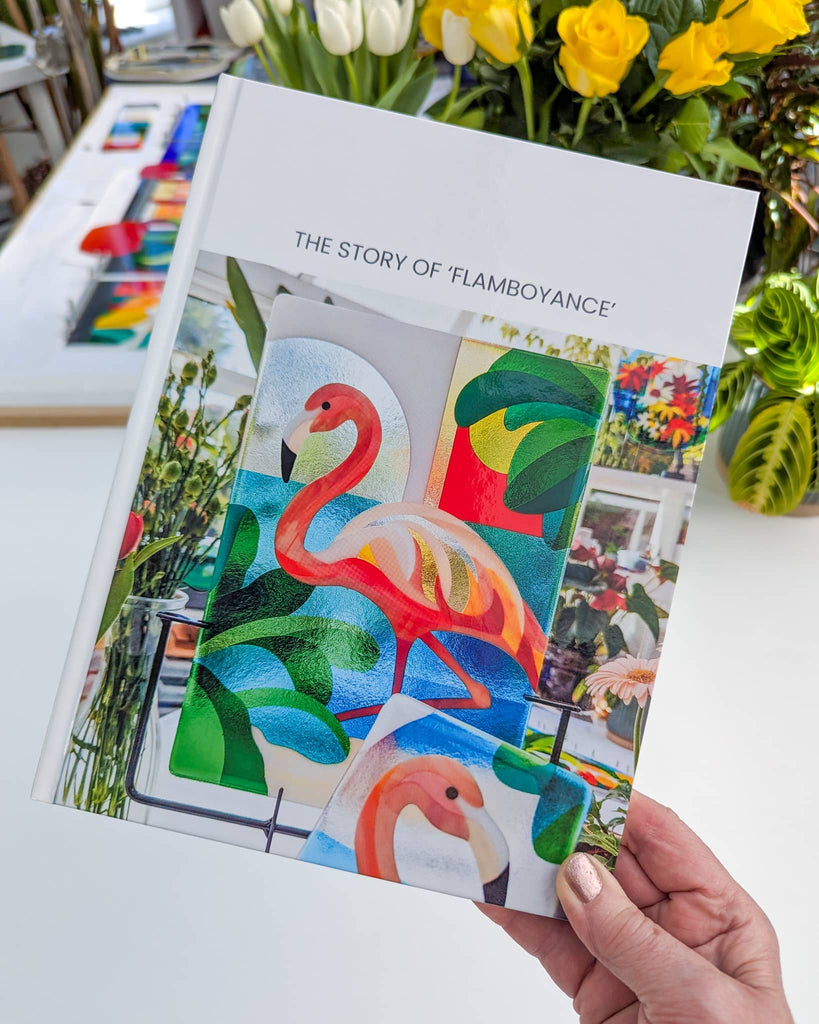 Hand holding a custom hardback book titled ‘The Story of Flamboyance’, featuring vivid photos of a commissioned flamingo-themed glass artwork – part of the personalised gift experience from Glass Art by Linda