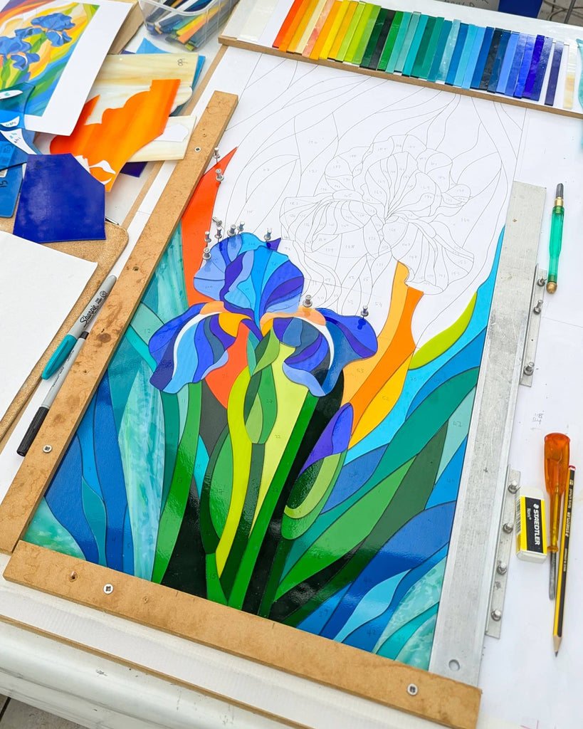 Work in progress layout for a fused glass panel featuring a large iris flower, with coloured glass pieces cut and placed on a design board – part of the creative process at Glass Art by Linda
