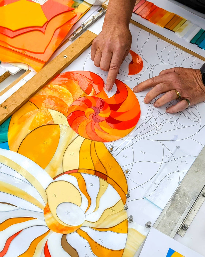 Work in progress creating the commissioned contemporary Hard Edge glass seashell artwork showing individually cut glass pieces assembled before kiln firing